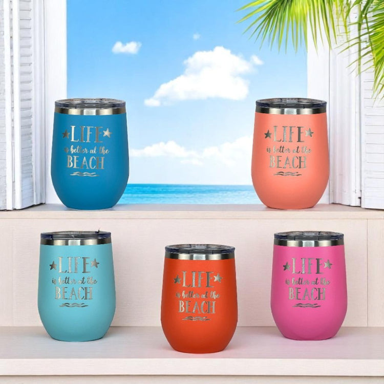 Assorted insulated beach wine tumblers in vibrant summer colors near a window with a beach view showcasing “Life is better at the beach” design.