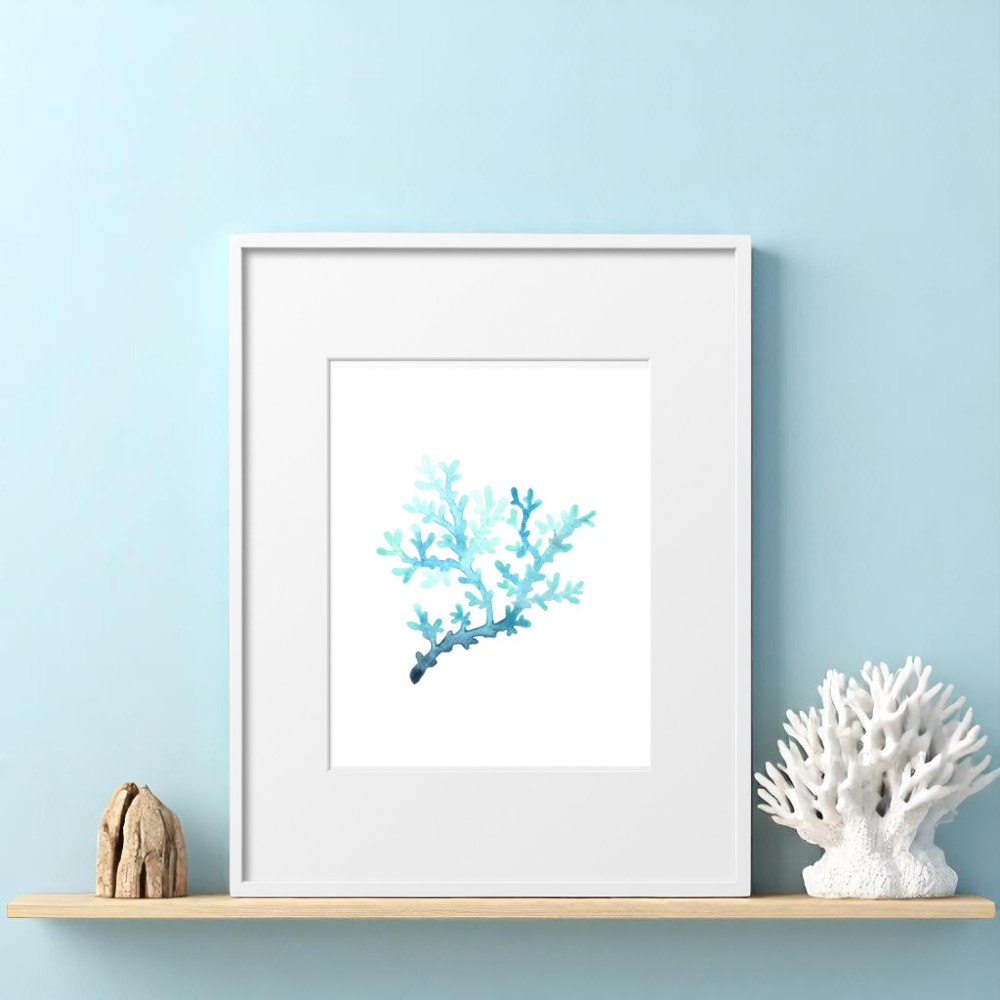ingle 8x10 framed coral art print leaning on a light wood shelf, styled with a white sculptural coral centerpiece and a piece of natural driftwood against a light blue wall in a coastal home setting.