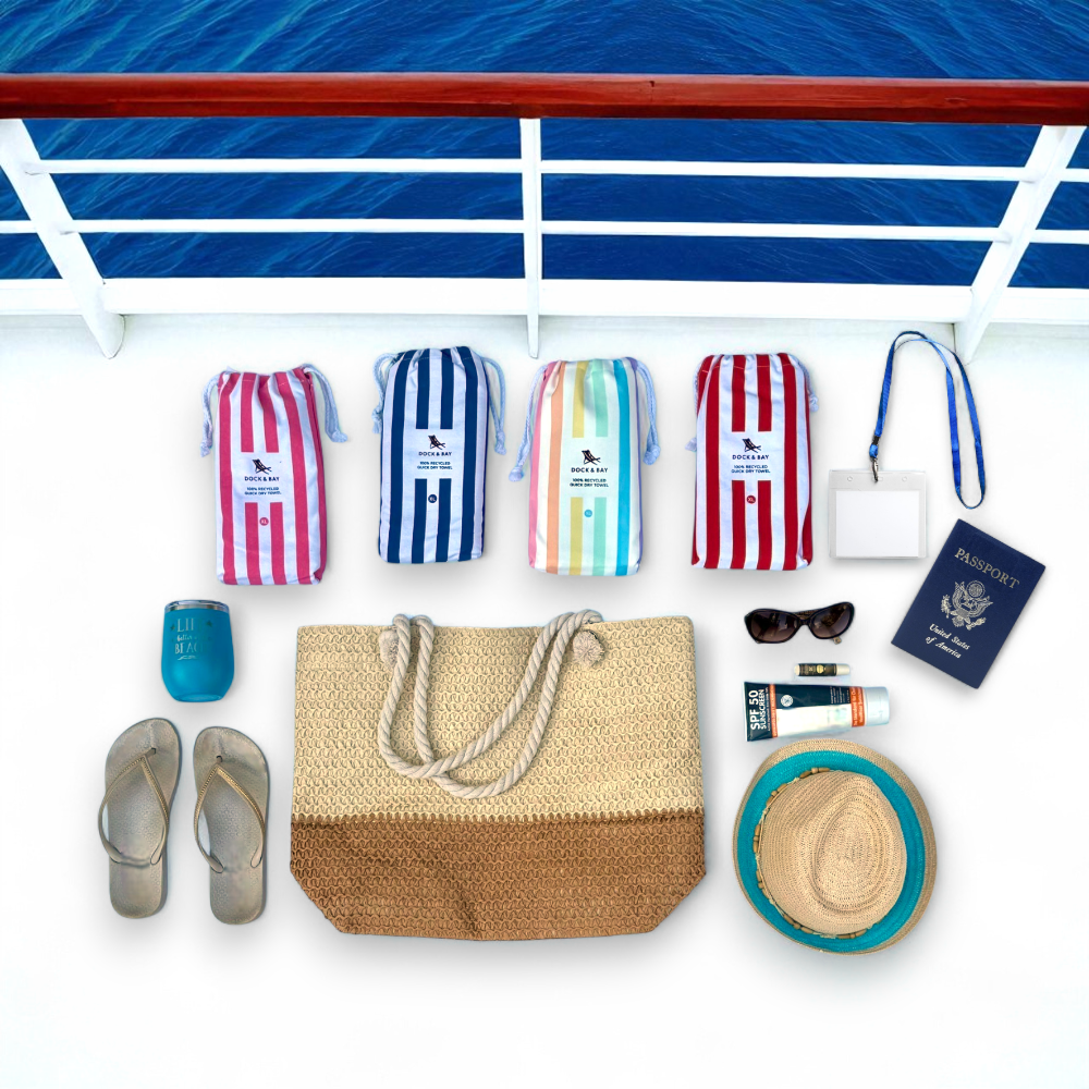 Flat lay of straw beach bag with cruise travel essentials including towels, hat, passport, sunscreen, and sunglasses