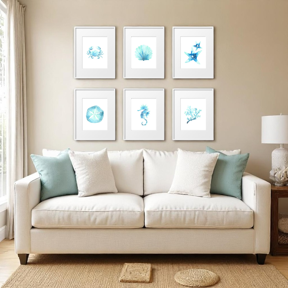 Six framed 8x10 beach art prints displayed above a cream couch in a neutral-toned coastal living room, styled with seafoam pillows, jute rug, and soft beach-inspired decor.