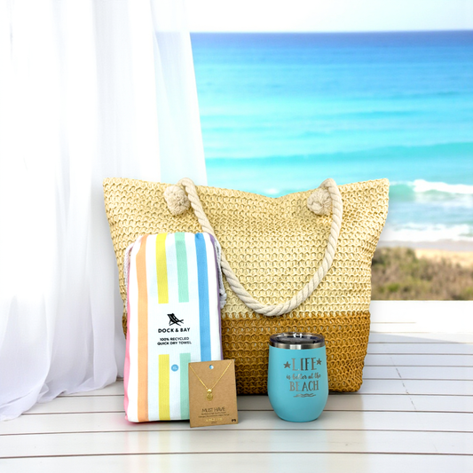 Pastel Beach Lover Gift Set with straw beach bag, pastel striped towel, teal beach tumbler, and gold pineapple necklace displayed on a white porch overlooking turquoise ocean water — the perfect coastal gift for beach lovers.