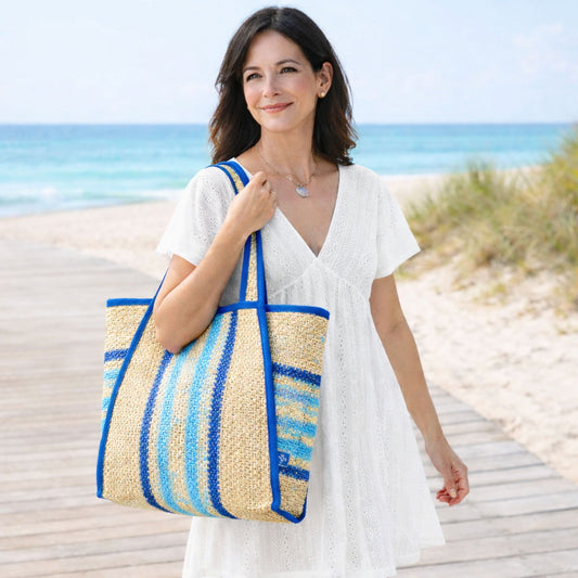 Woman carrying a blue striped straw beach tote bag with blue trim and aqua stripes on a beach boardwalk