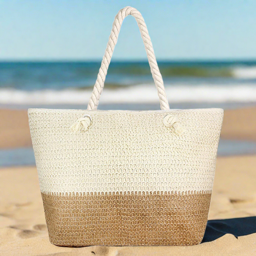 Beige and tan beach bag with rope handles placed near shoreline waves