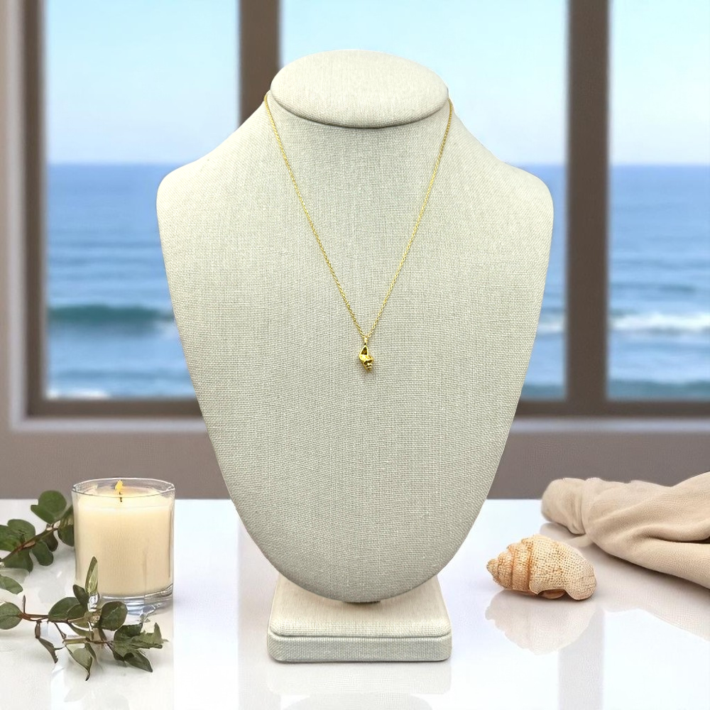 Conch shell pendant necklace displayed on a linen jewelry bust with a spa-inspired coastal vanity setup including a beach-scented candle and dried eucalyptus.