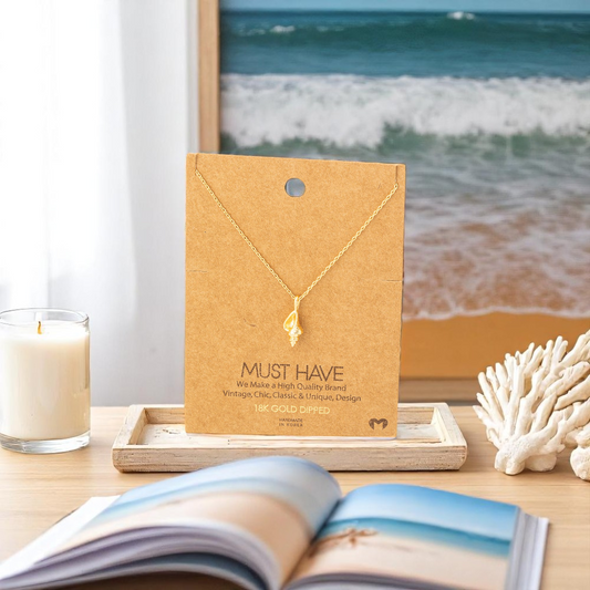 conch shell 18k gold dipped necklace on dresser with beach photo, book and coral