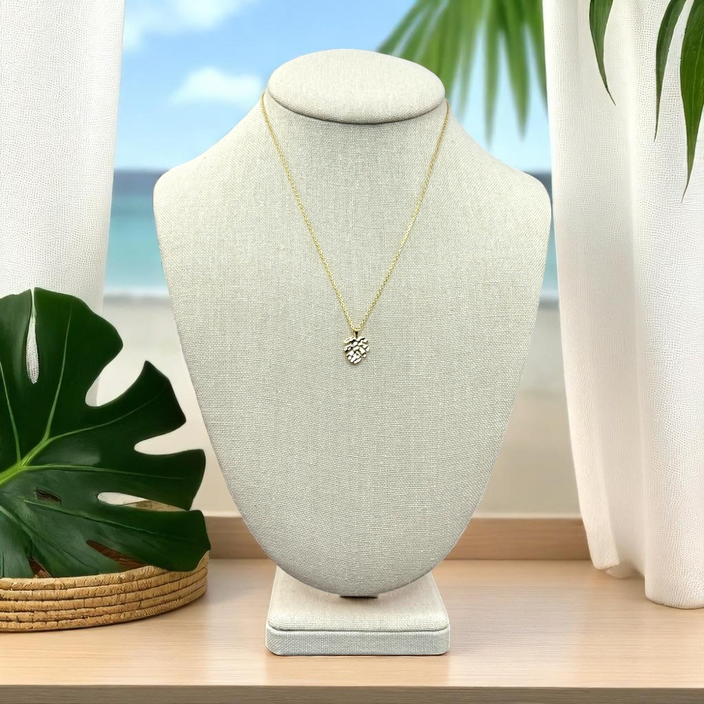 Linen jewelry bust on a rattan tray or light wood shelf. The monstera leaf necklace is centered on the bust. Add a monstera leaf beside it, with light shadows and a white linen backdrop. Fresh, airy, and botanical beach view.
