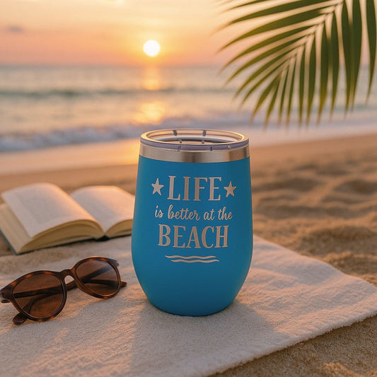 ocean blue metal insulated wine tumbler in a beach sunset setting with a beach blanket, book and sunglasses