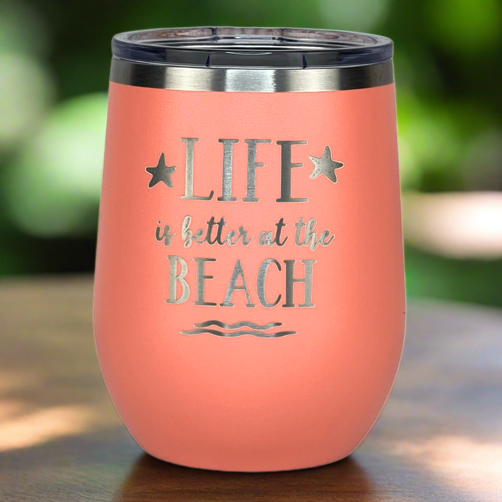 Peach "Life is Better at the Beach" tumbler on a wooden table, with a tropical background