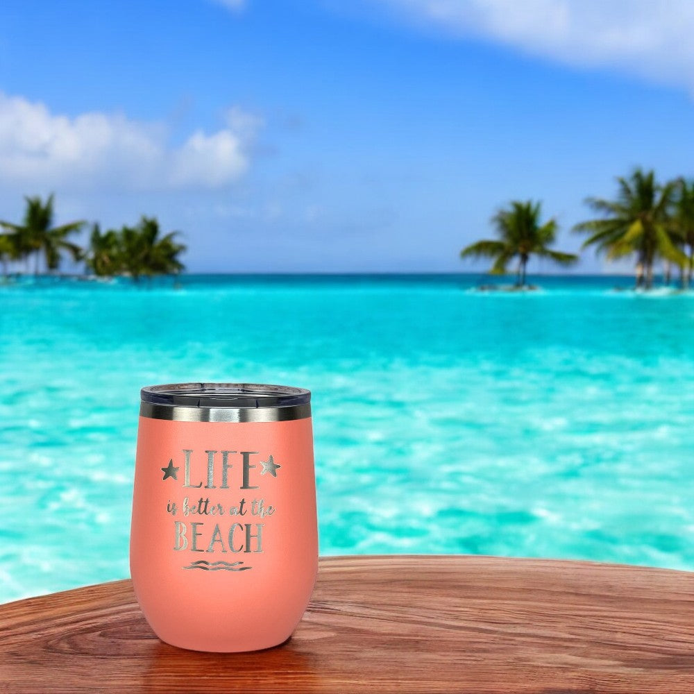 Peach metal drink tumbler with lid, perfect for beach lovers sitting on a wooden table with an ocean view