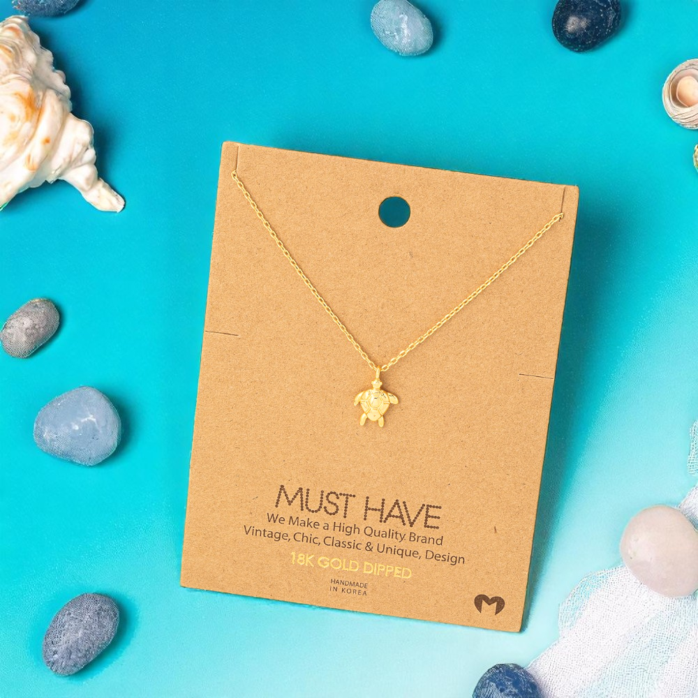 Gold turtle necklace on a brown card with seashell and stone decorations on a blue background