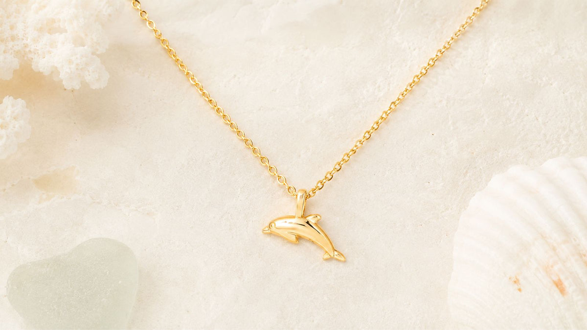 	 Dainty 18k gold dolphin necklace on a sandy background from Breezy Cove