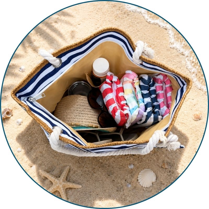 Large navy and white striped beach bag filled with towels, sunscreen, and flip flops on a bright beach day.