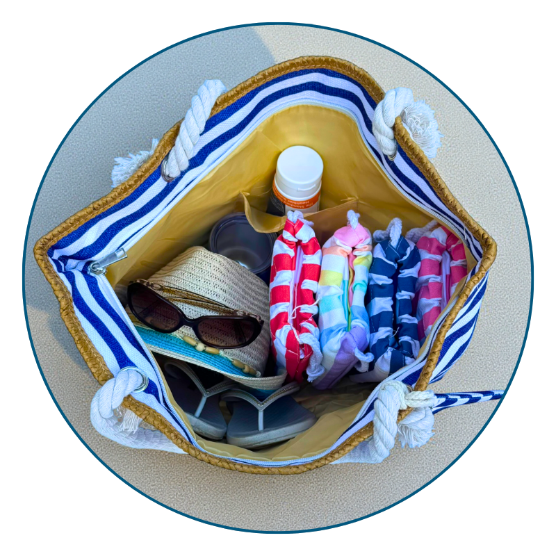 Large navy and white striped beach bag filled with towels, sunscreen, and flip flops on a bright beach day.