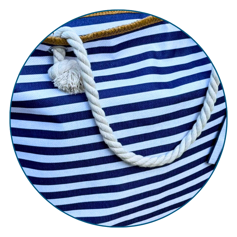 Close-up of soft rope handles on a navy and white striped beach bag against a coastal background.