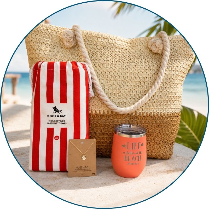 Coral beach lover gift set styled by the ocean with straw beach bag, striped towel, peach tumbler and gold-dipped monstera necklace.
