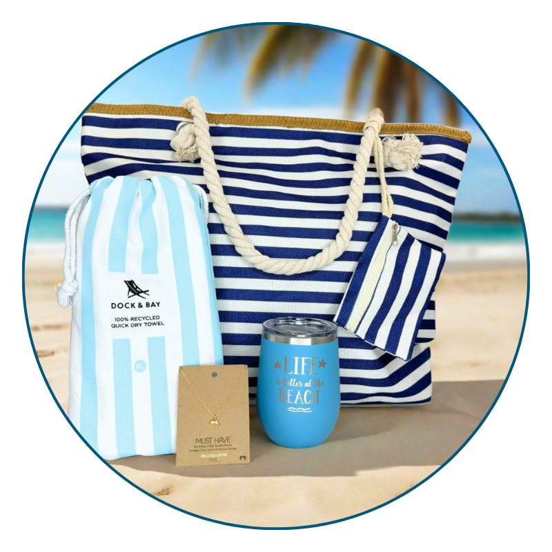 light blue nautical beach lover gift set including a striped bag, towel, and tumbler on a sandy beach with a ocean background.