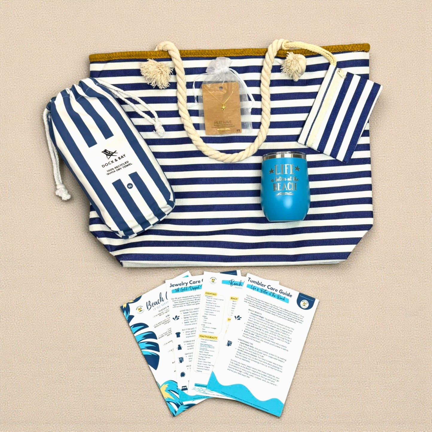 Flat lay of Navy Nautical Beach Lover Gift Set with striped beach bag, navy striped beach towel, ocean blue wine tumbler, sea turtle necklace, and bonus cards.
