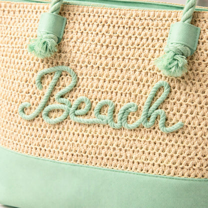 Close-up of mint green raised “Beach” lettering, rope handles, and zipper on straw tote bag