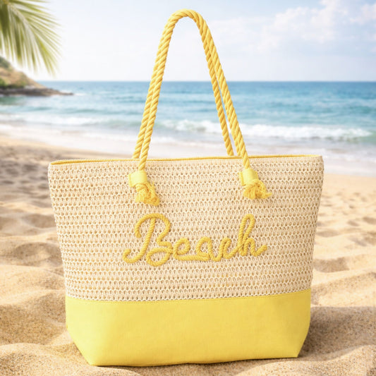 Yellow straw beach tote bag with “Beach” message on sand with ocean background
