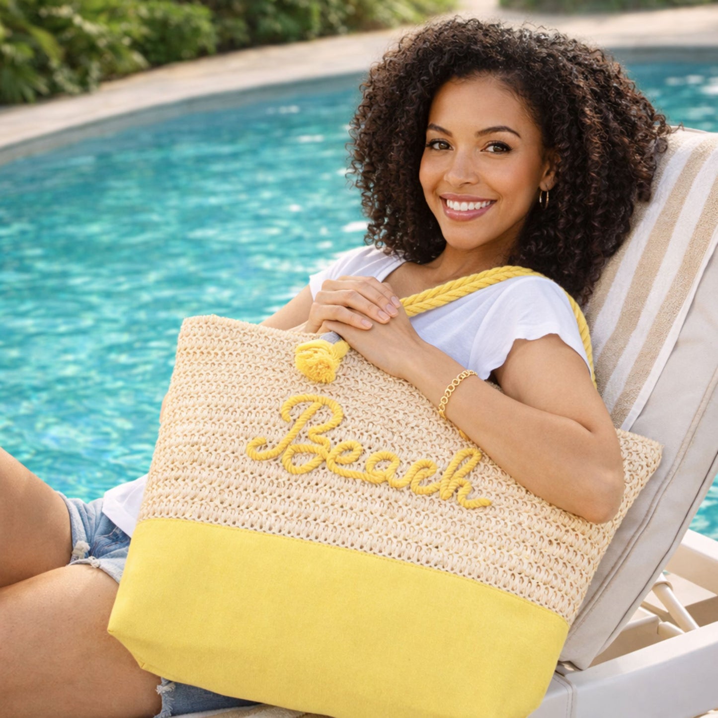 Woman lounging by pool holding yellow straw beach tote bag with rope handles and “Beach” message