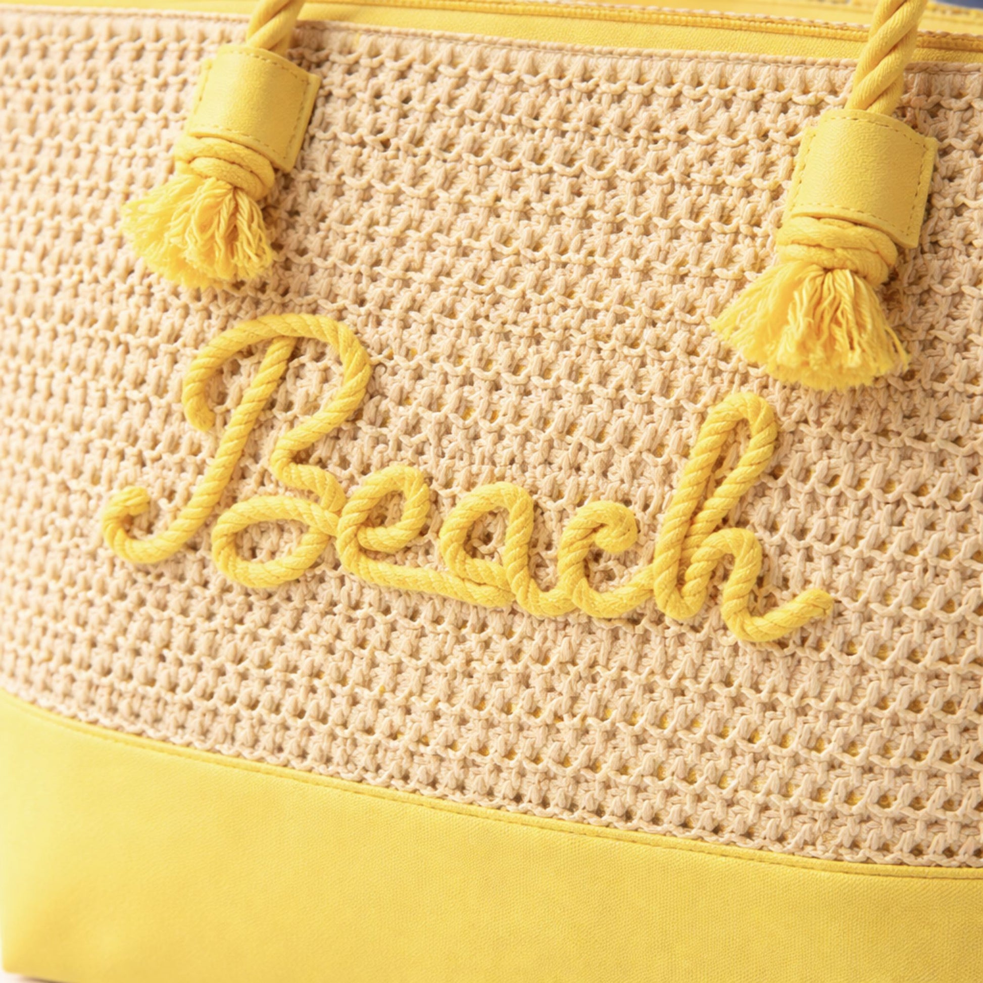 Close-up of yellow “Beach” rope embroidery and zipper top on straw canvas tote bag