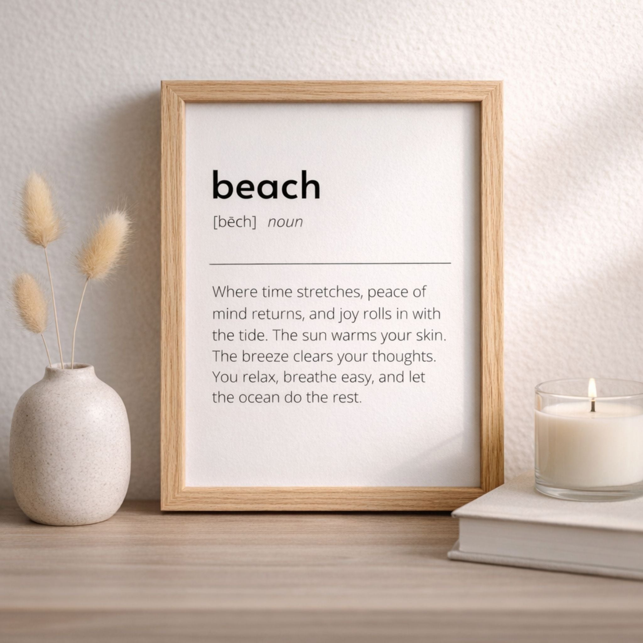 Framed beach definition art print with neutral vase and candle in a calm coastal decor setting