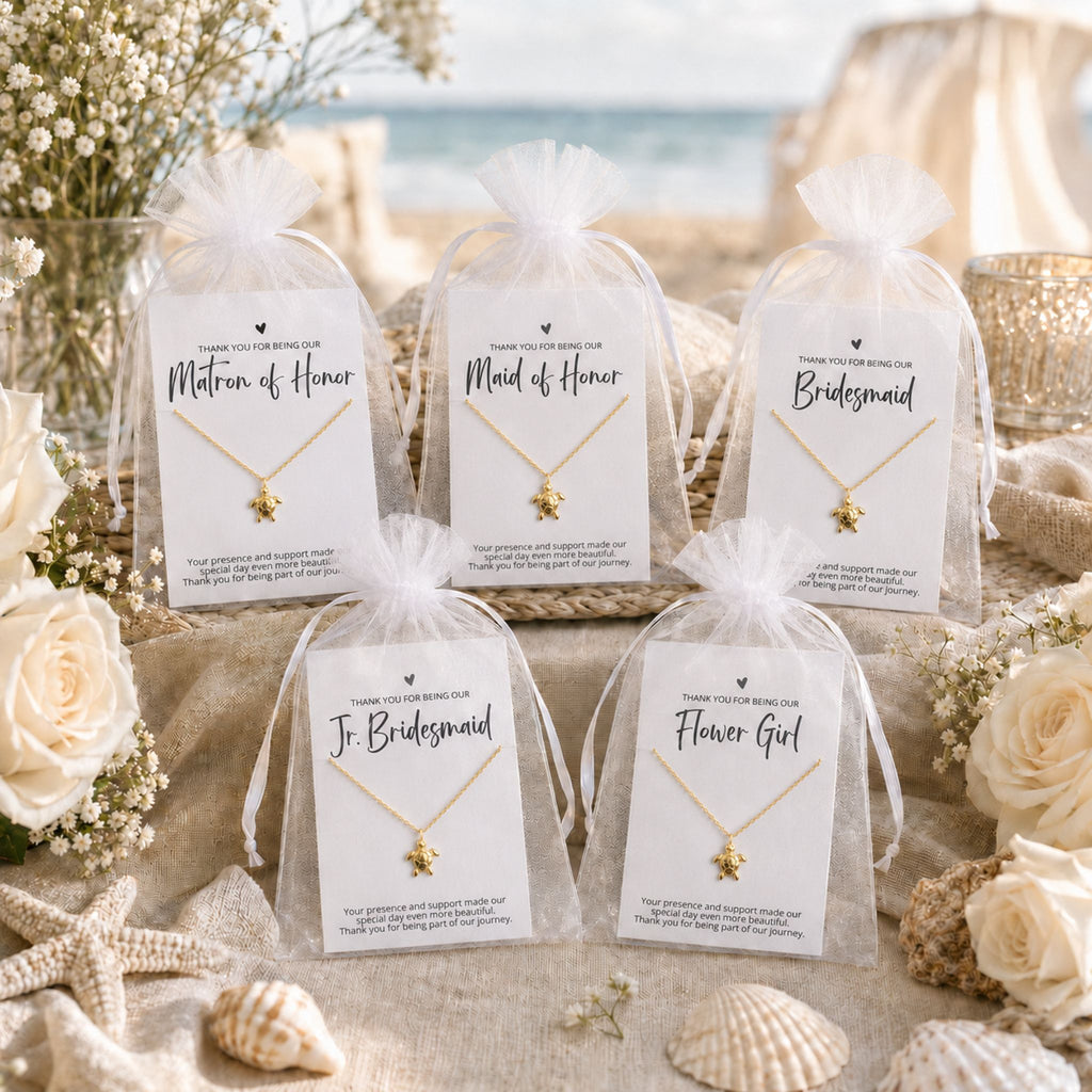 Beach wedding bridal party gifts displayed with coastal sea turtle necklace cards and white organza bags on a beach gift table