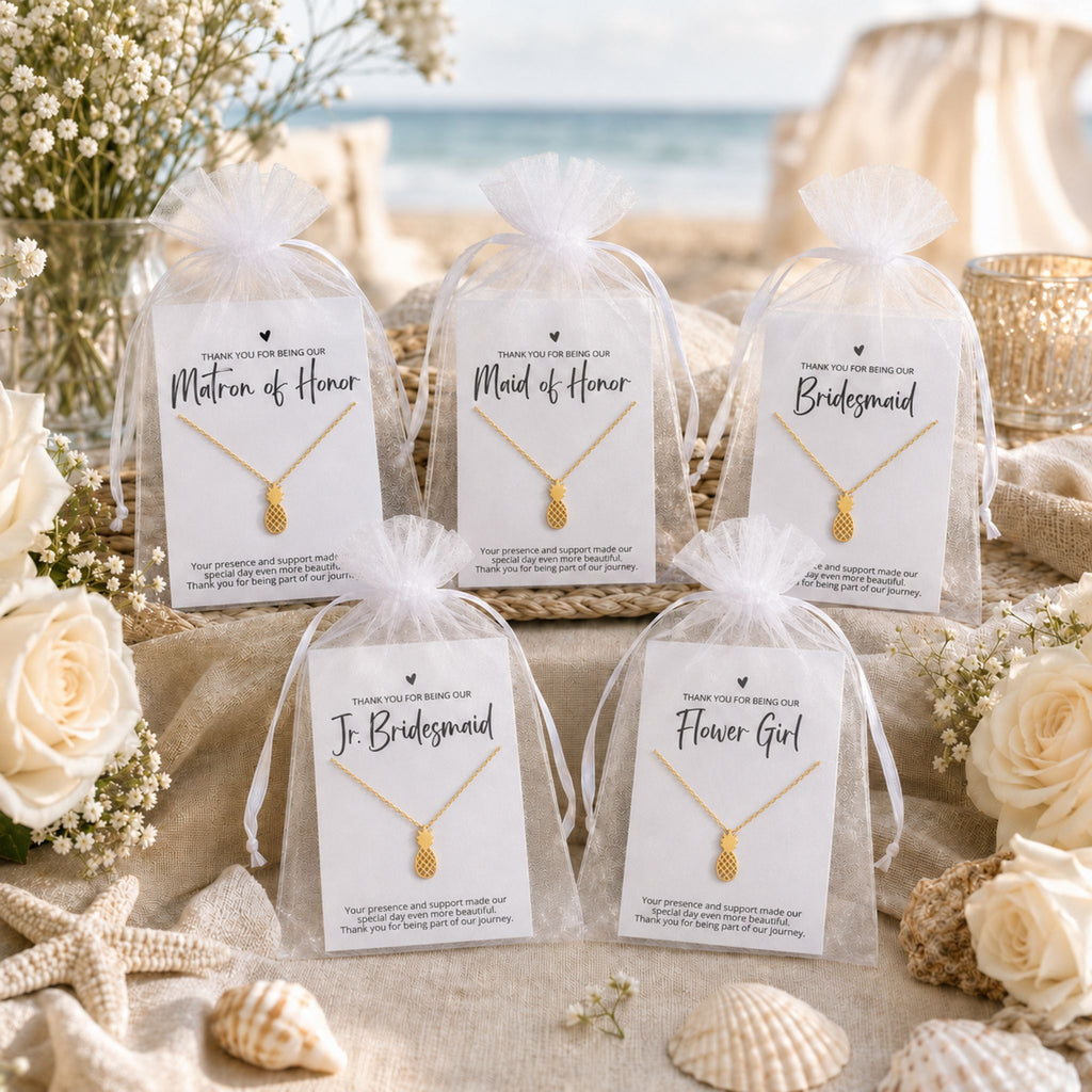Beach wedding bridal party gifts displayed with coastal pineapple necklace cards and white organza bags on a beach gift table