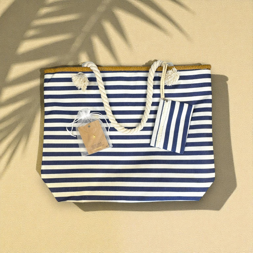 Flat lay of navy striped beach bag and gold sea turtle necklace on sandy background with palm leaf shadows — Breezy Cove Best Seller Bundle capturing effortless tropical coastal style.