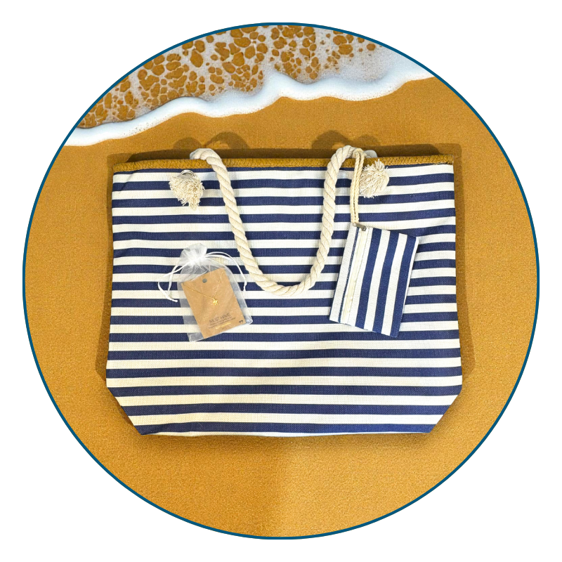 Coastal best seller bundle with navy striped beach bag and 18k gold sea turtle necklace flat lay on sand with ocean on the edge