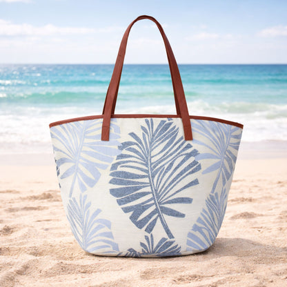 Blue palm leaves canvas beach bag tote with zipper on sand at the beach.
