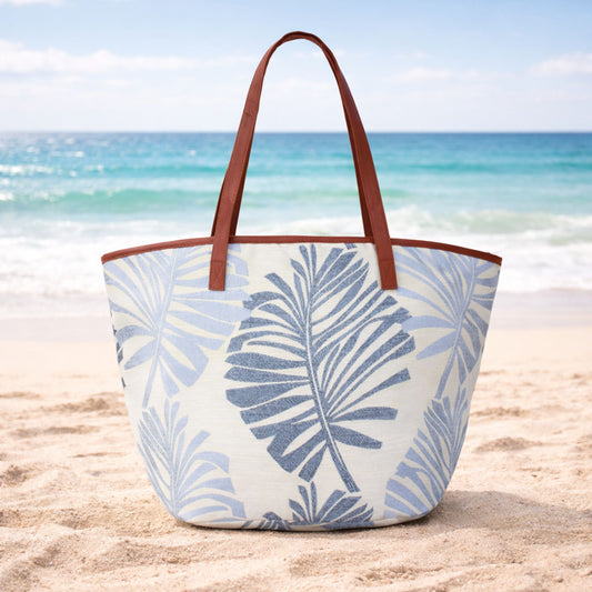 Blue palm leaves canvas beach bag tote with zipper on sand at the beach.