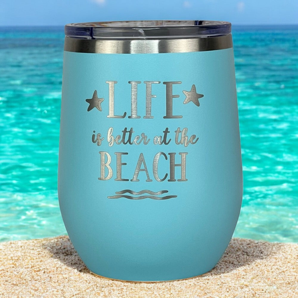 Teal insulated tumbler with lid on a sandy beach