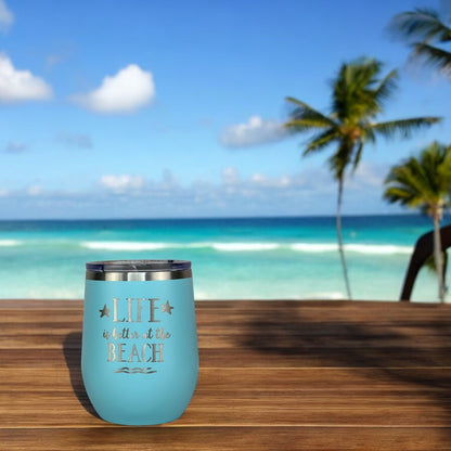 Teal beach tumbler with secure lid placed on a beachside table