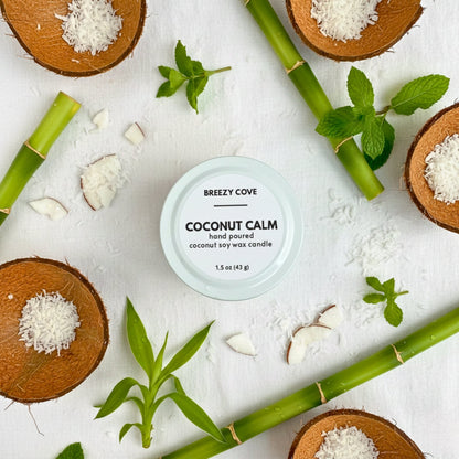 Coconut Calm coconut beach candle surrounded by coconut pieces and fresh greenery in a tropical flat lay.