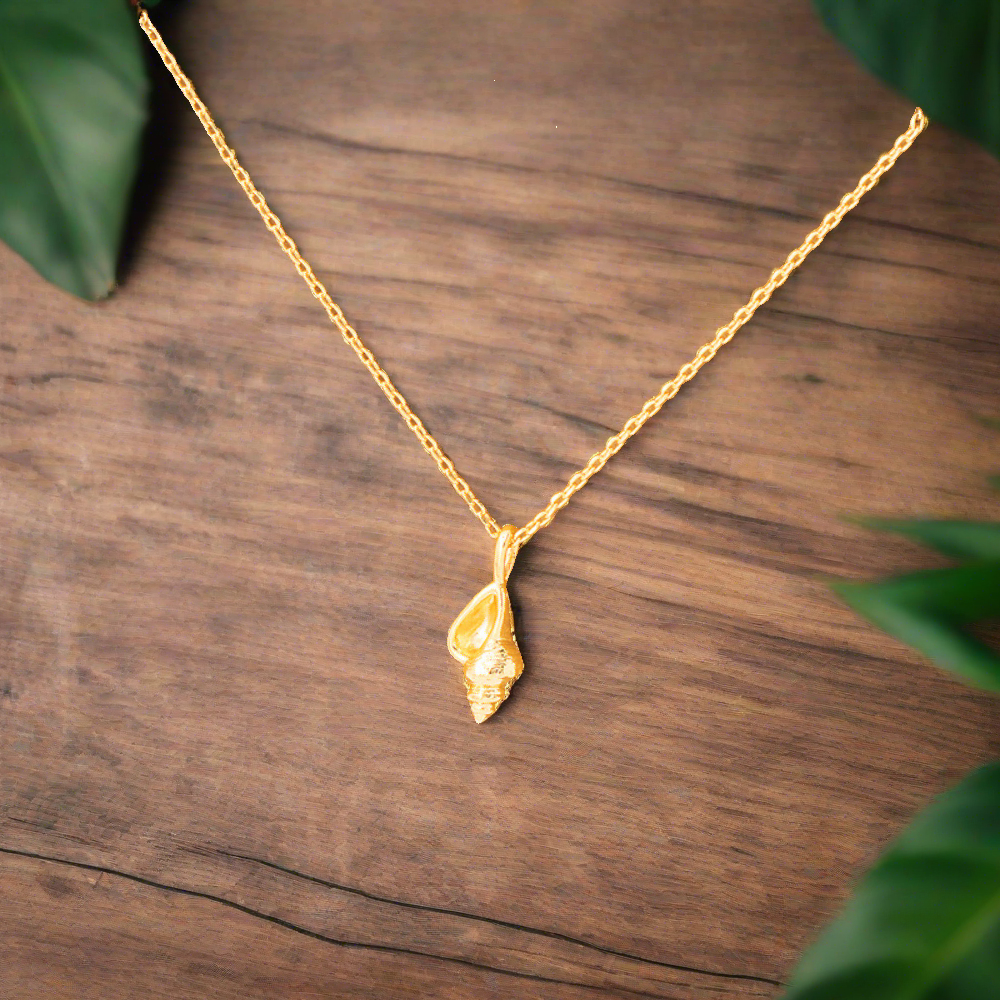 dainty, conch seashell pendant 18k gold dipped necklace is perfect accessory for beach lovers, laying on walnut table with palm leafs