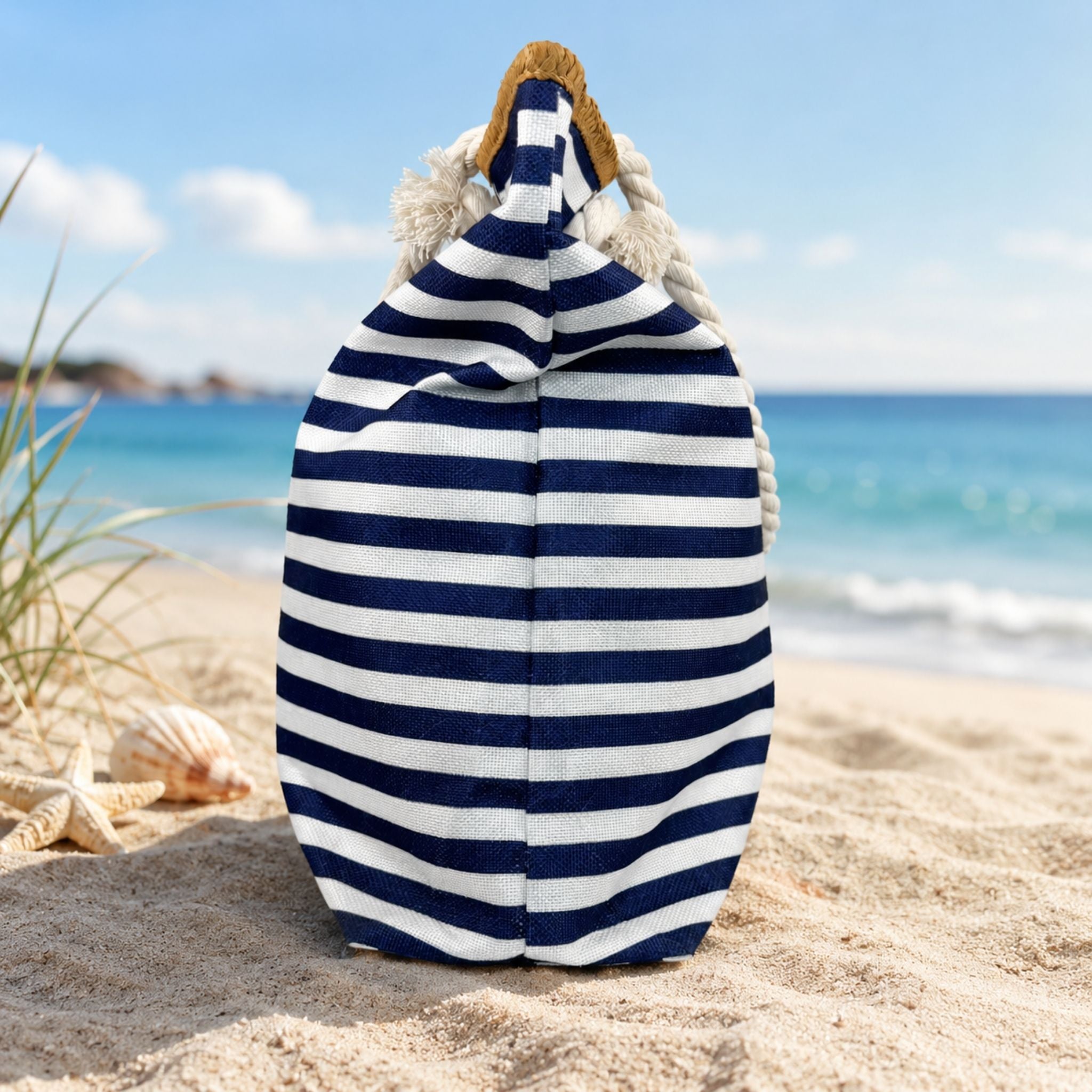 The side view of a cute, navy and white striped beach bag with zipper on a sandy beach with ocean view