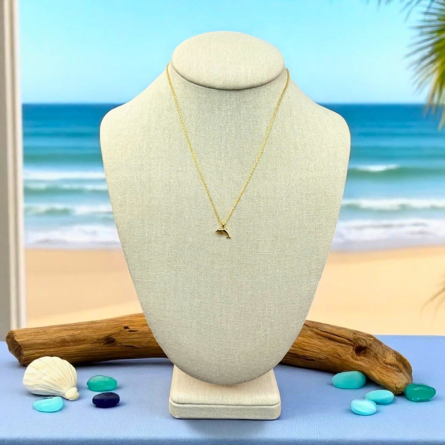 dainty gold dolphin beach Necklace on a mannequin bust with a beach background