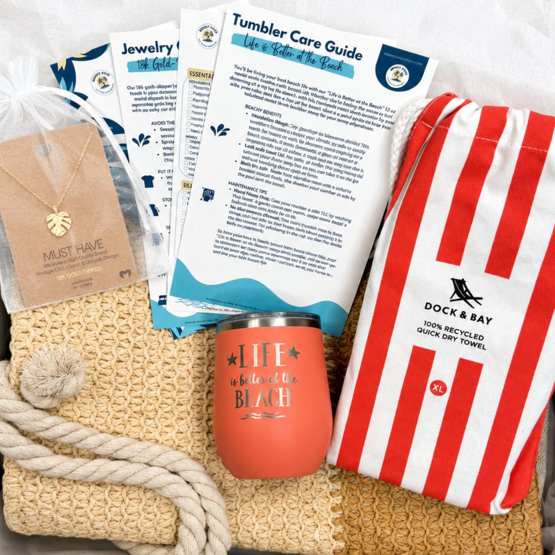 Gift-ready coral beach gift set boxed with straw beach bag, coral striped towel, peach tumbler, gold-dipped monstera necklace and bonus cards.