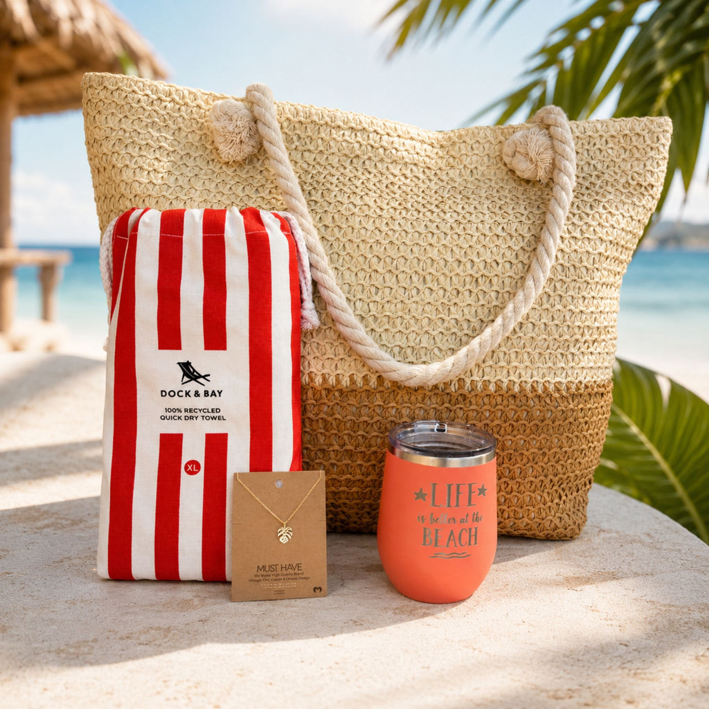 Coral beach bag gift set for beach lovers with straw tote, striped beach towel, tumbler and gold dipped necklace by the ocean.