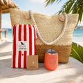 Coral beach bag gift set for beach lovers with straw tote, striped beach towel, tumbler and gold dipped necklace by the ocean.