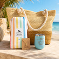 Pastel beach bag gift set for beach lovers with straw beach bag, pastel striped towel, blue tumbler and gold-dipped pineapple necklace by the ocean.