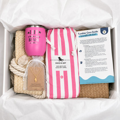 Pink beach gift set for beach lovers with straw beach bag, pink quick dry towel, pink tumbler, conch shell necklace, and care cards packaged in a gift box with tissue paper.