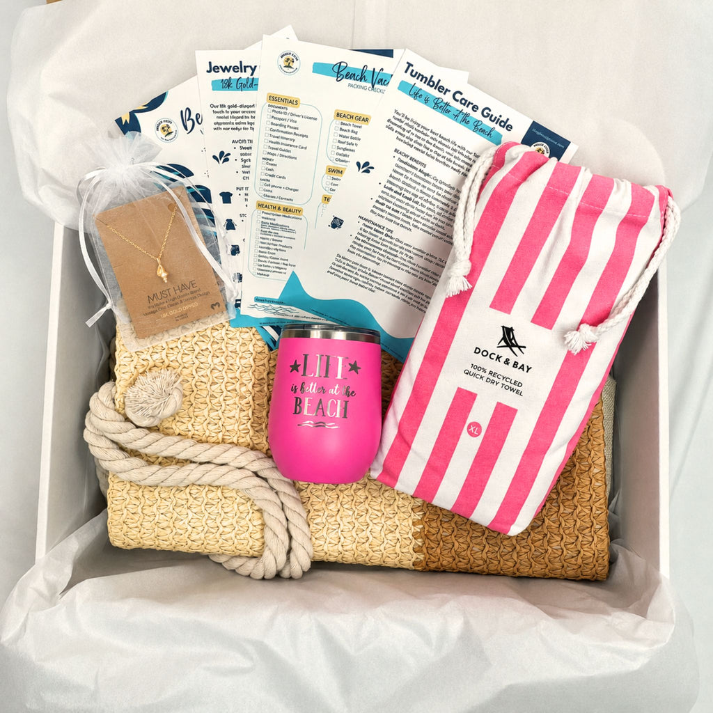 Pink beach gift set for beach lovers with straw beach bag, pink striped quick dry towel, pink tumbler, and gold dipped conch shell necklace packaged in a gift box with tissue paper