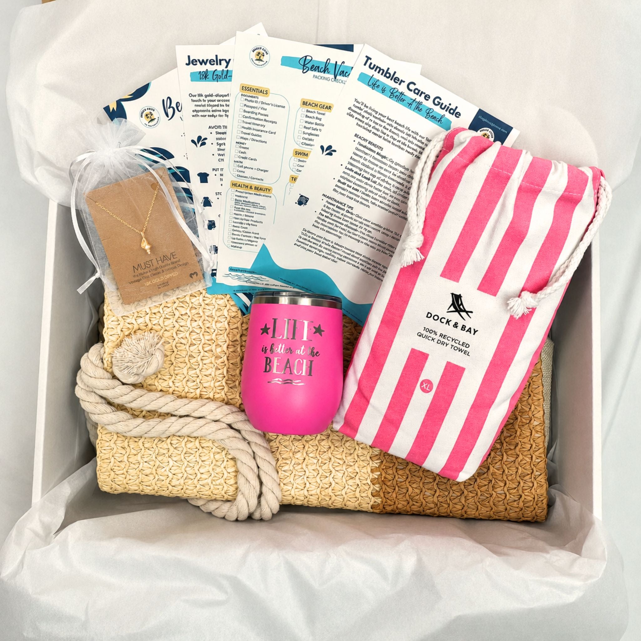 Pink beach gift set for beach lovers with straw beach bag, pink striped quick dry towel, pink tumbler, and gold dipped conch shell necklace packaged in a gift box with tissue paper