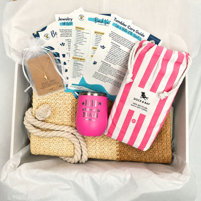 Pink beach gift set for beach lovers with straw beach bag, pink striped quick dry towel, pink tumbler, and gold dipped conch shell necklace packaged in a gift box with tissue paper