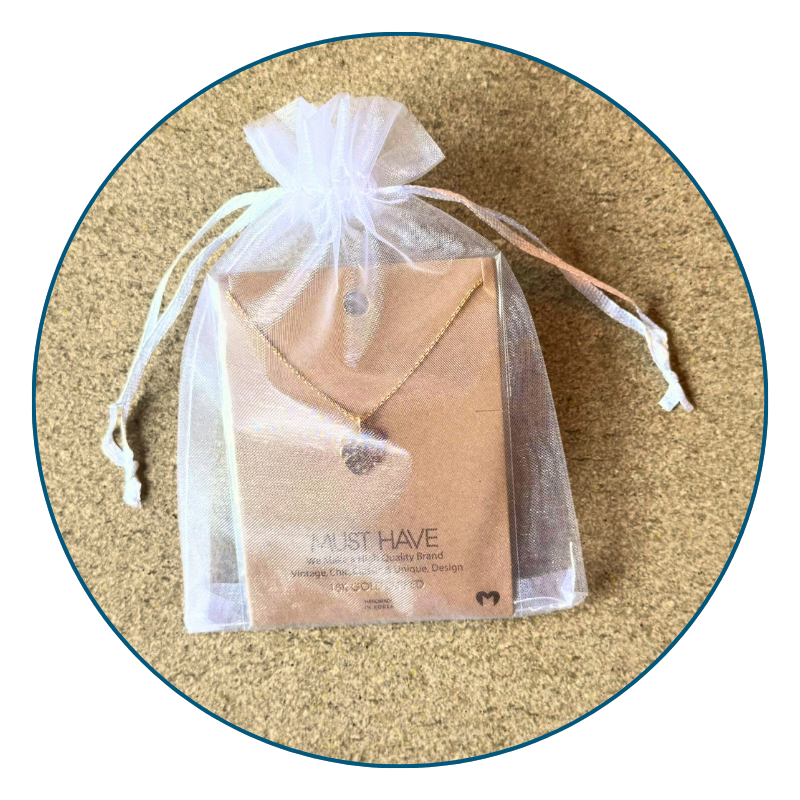Gold monstera necklace in sheer white organza gift bag with ribbon, perfect for gifting or safe storage.
