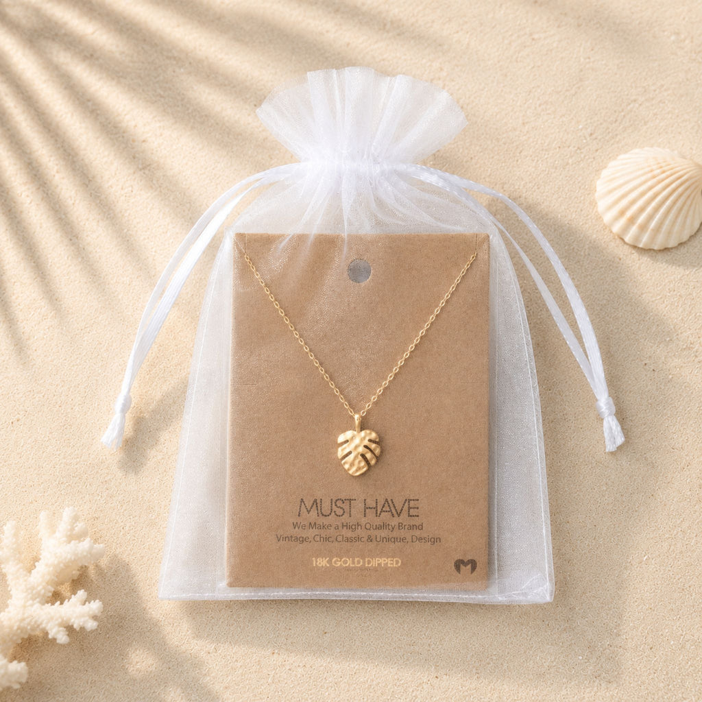 Gold monstera leaf pendant necklace in and white organza bag for unique gifts for beach lovers