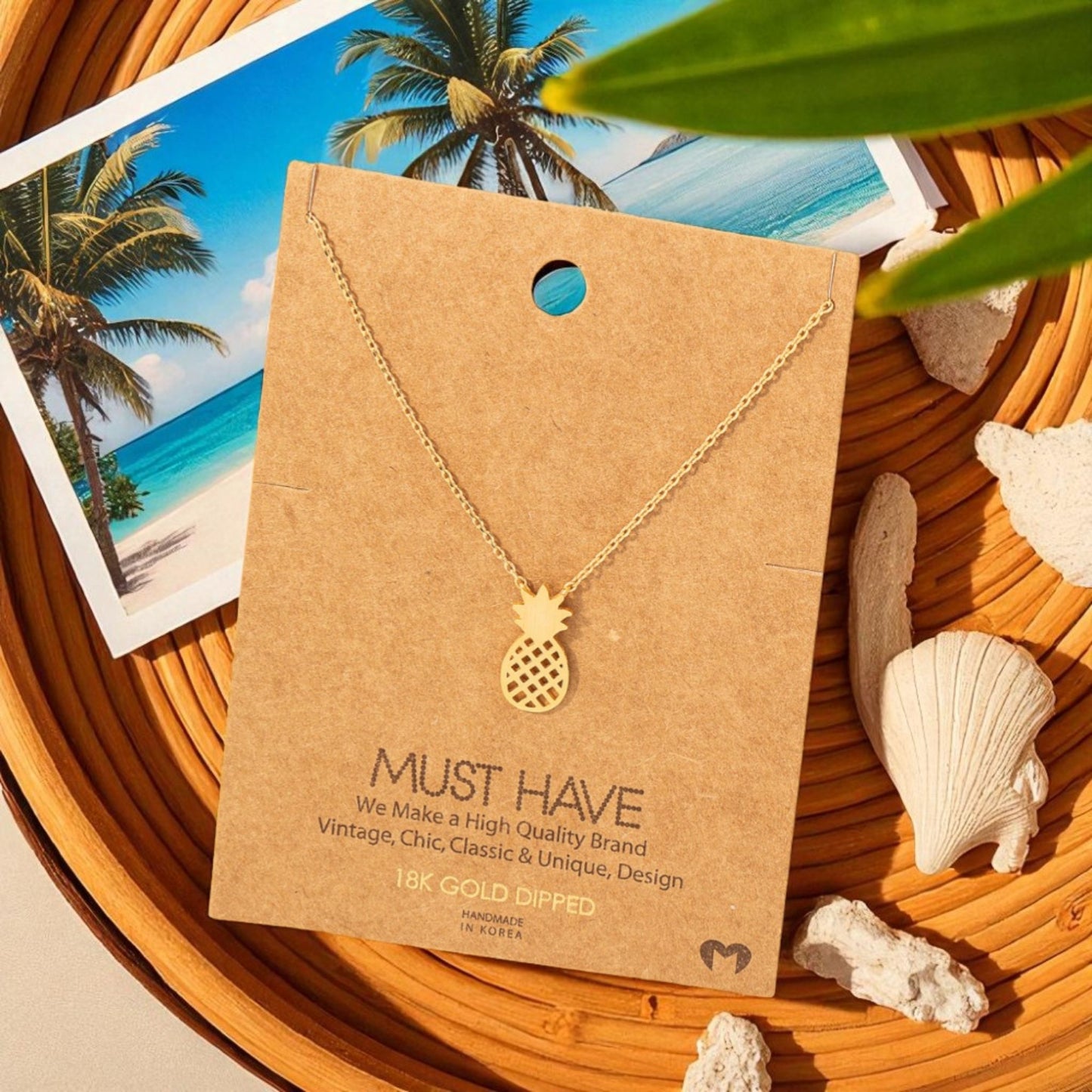 Gold pineapple necklace on a brown card with beach-themed background