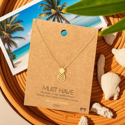 Gold pineapple necklace on a brown card with beach-themed background